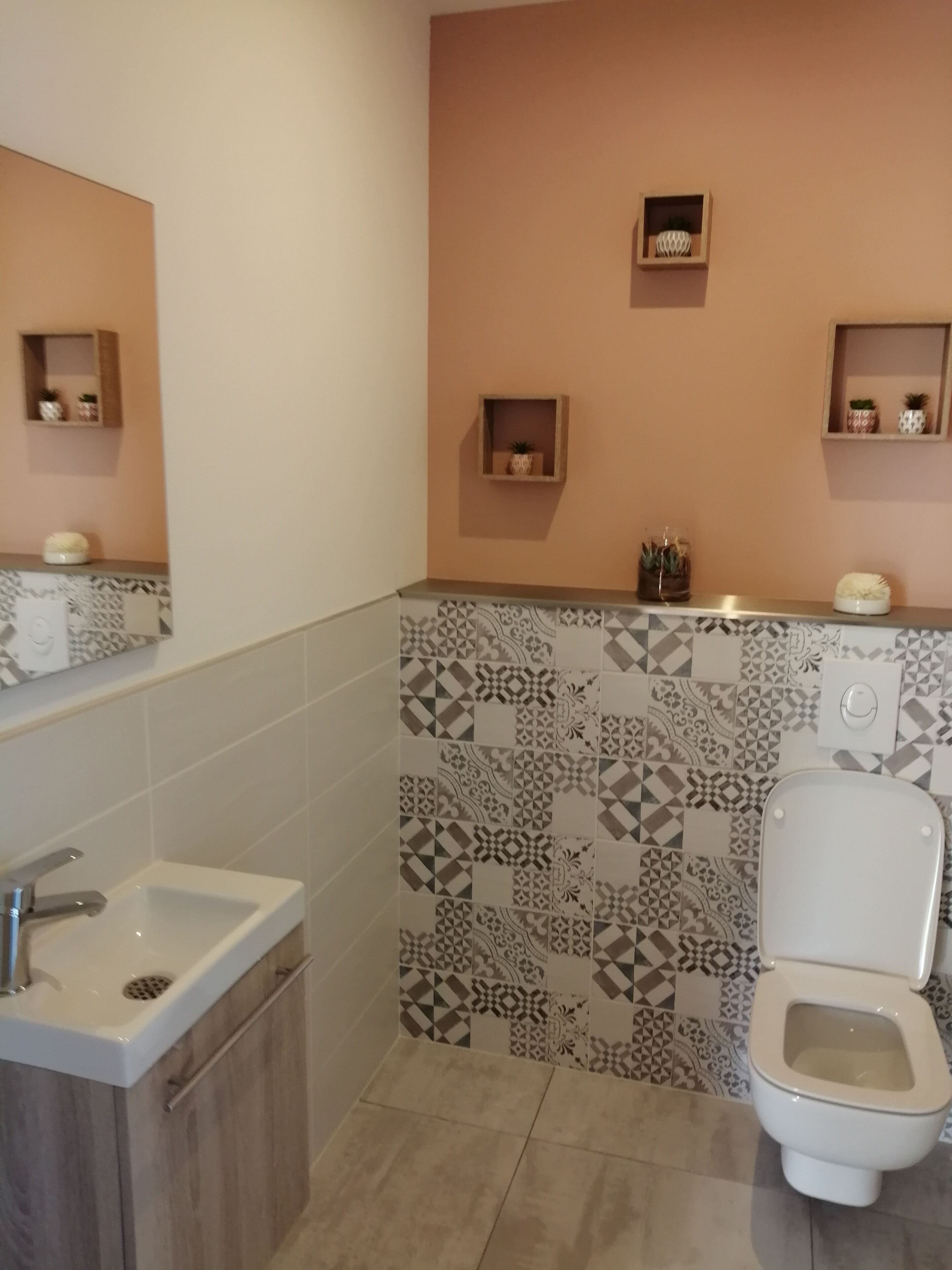 A bathroom with a white sink, a toilet, and patterned tiles on the walls.