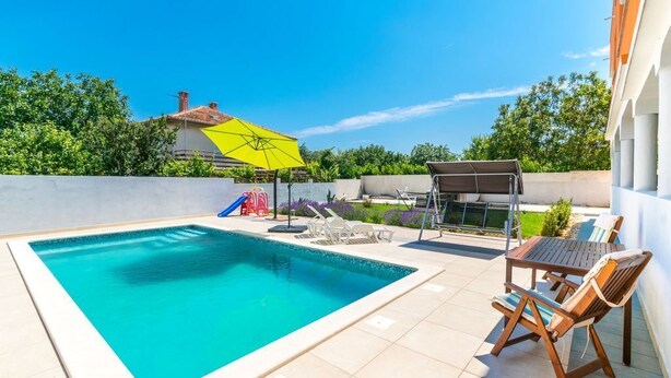 A swimming pool with a tiled deck, a sun umbrella, and outdoor furniture. - Affordable Janko Apartment (Medulin)