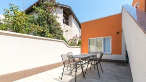 An outdoor patio with a table and chairs, a white wall, and a building with orange and beige walls. - Affordable Janko Apartment (Medulin)
