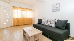 A modern living room with a grey sofa, a wooden coffee table, and a window with yellow curtains. - Affordable Janko Apartment (Medulin)