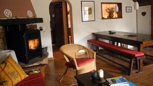 Un salon chaleureux avec une cheminée, un fauteuil en osier, un banc et une table à manger.
