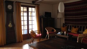 Un salon chaleureux avec une table en bois, des chaises, un canapé et une grande fenêtre agrémentée de rideaux.