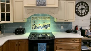 A kitchen with white cabinets, a blue backsplash, a clock, and a stove.