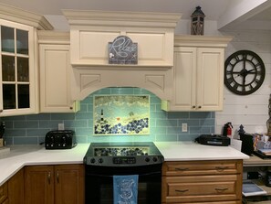Una cocina con armarios blancos, salpicadero azul, un reloj y una estufa.