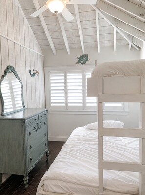 Quarto com uma cama de solteiro e solteira, cômoda, ventoinha no teto e janela com persianas.