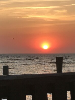 Ein Sonnenuntergang über dem Meer mit einem hölzernen Geländer im Vordergrund.