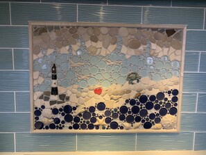 Eine Mosaikwand mit einem Leuchtturm, Muscheln und einem Herz.