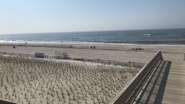 A beach with a wooden boardwalk and a sandy area with sparse vegetation.