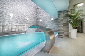 A modern indoor pool with a curved water feature, tiled walls, and a potted plant. - Admirał I (Swinoujscie)