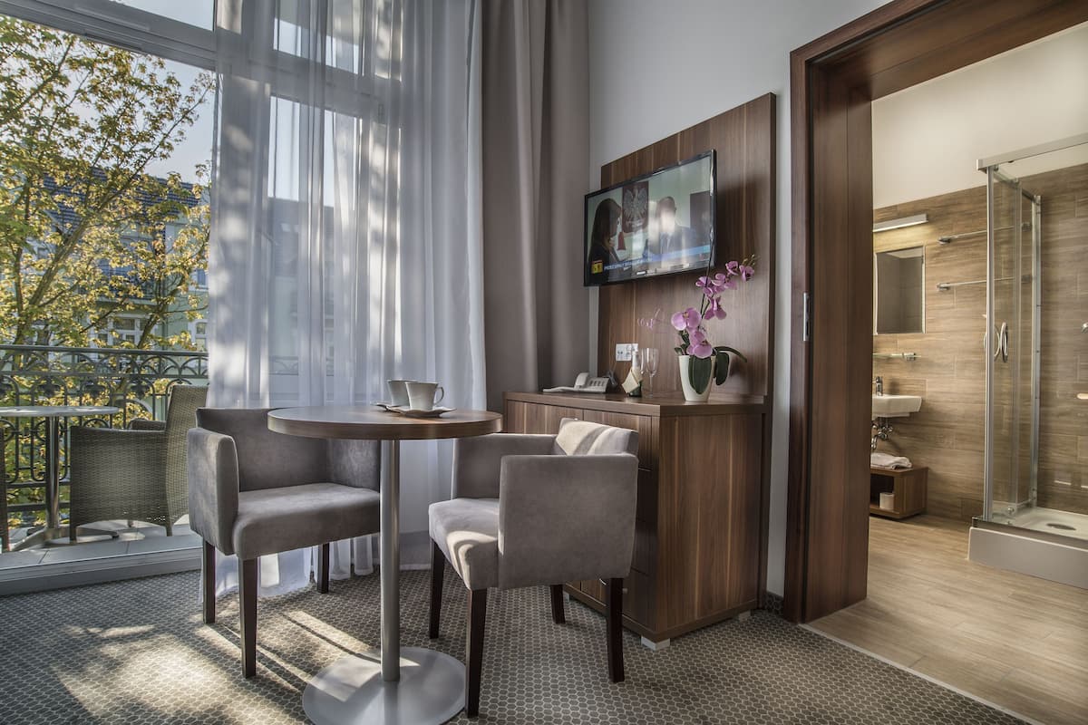 Ein modernes Hotelzimmer mit Balkon, einem Wand-Fernseher, einem kleinen Schreibtisch mit Stuhl und einer Duschkabine.