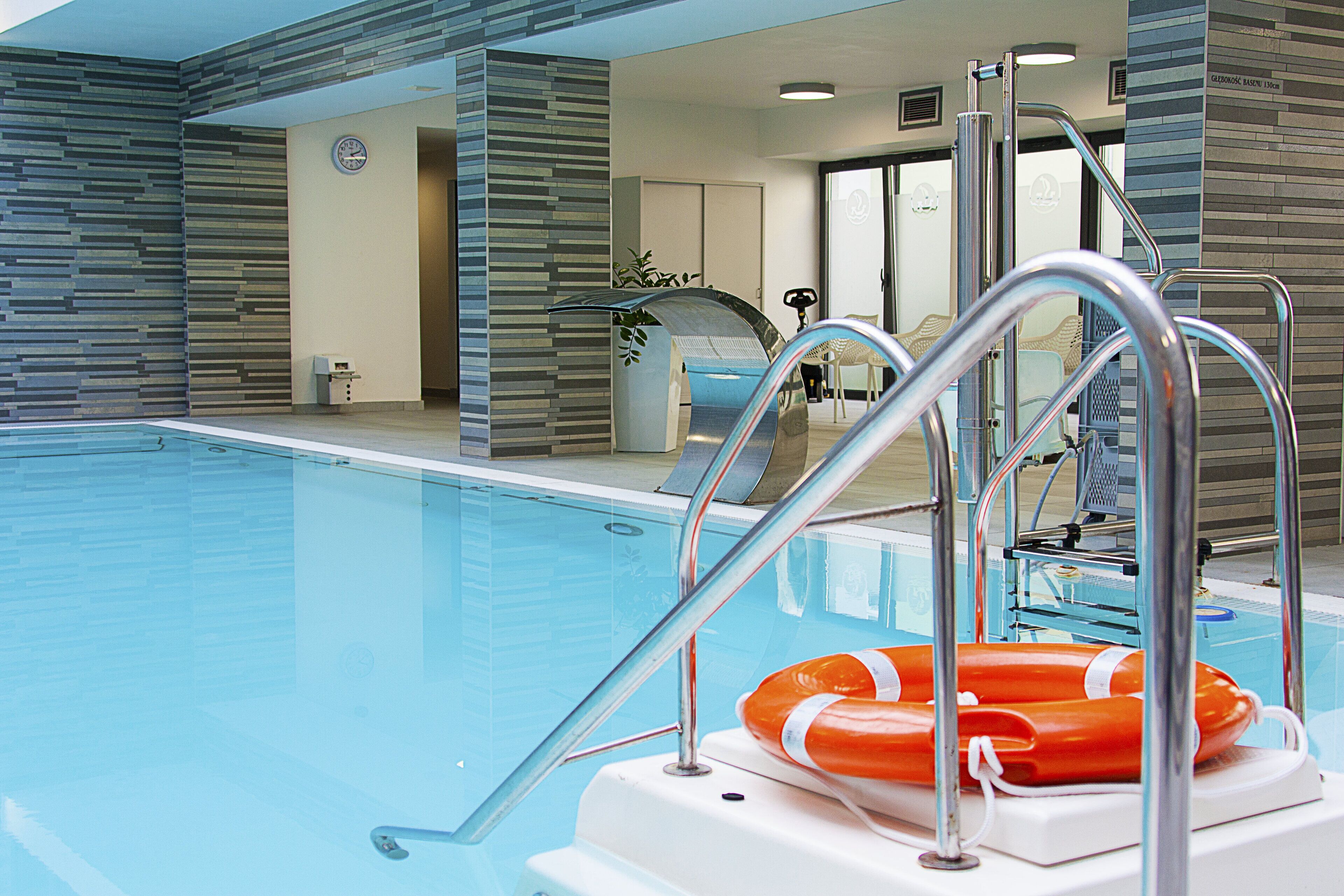 An indoor swimming pool with clear water, metal pool ladders, and a lifebuoy.