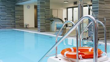 An indoor swimming pool with clear water, metal pool ladders, and a lifebuoy.