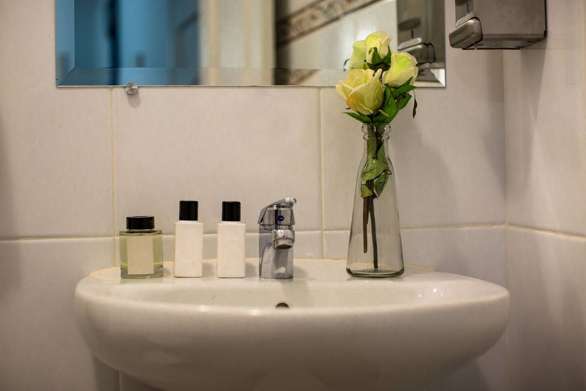 A bathroom sink with a mirror, a vase with flowers, and three bottles of liquid.