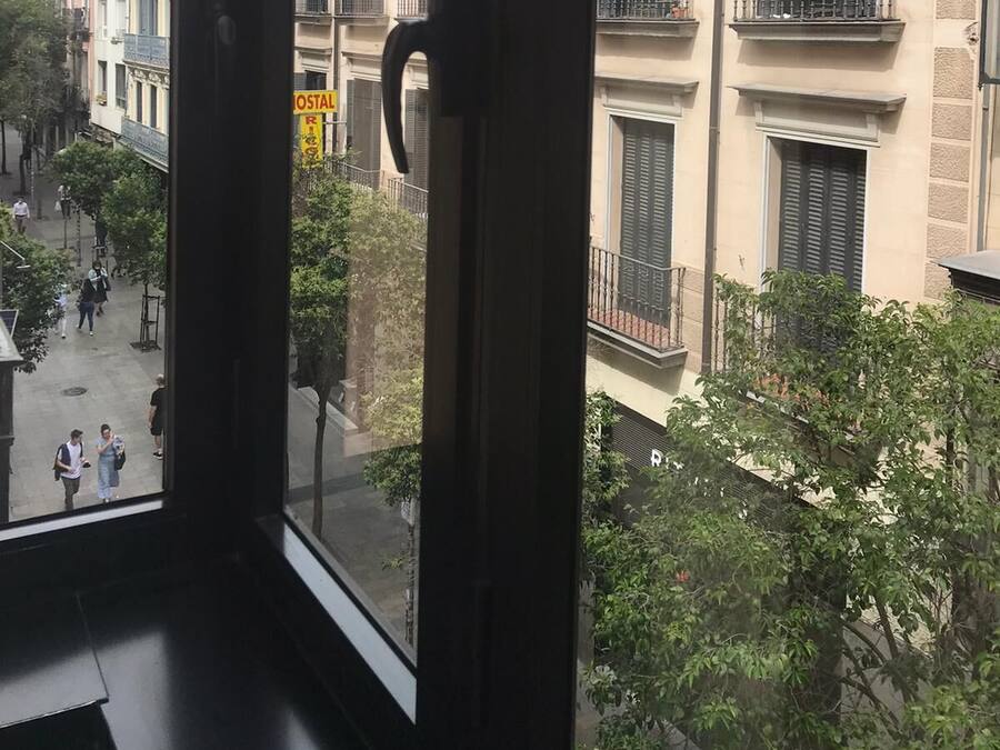 Vista da janela com puxador, mostrando uma rua com edifícios, árvores e pessoas a pé.