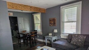 Un salon avec un canapé gris, une table basse en bois et un coin repas comprenant une table et des chaises en bois.