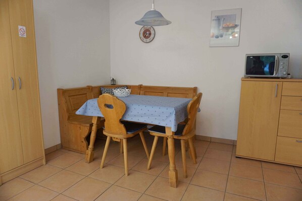 A dining area with a wooden table and chairs, a microwave on a cabinet, and a clock on the wall.