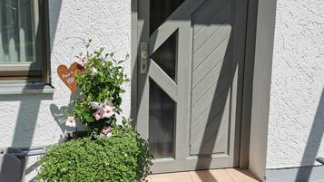 Eine Tür mit diagonalem Muster, einer Fußmatte und einem kleinen Topf mit rosa Blüten.