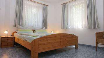 Ein Schlafzimmer mit einem Holzbett, zwei Nachttischen mit Lampen, einem Sessel und Vorhängen an den Fenstern.