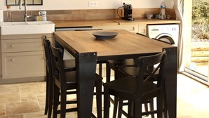 Una cocina moderna con una mesa de madera, sillas negras, horno empotrado y un ventanal grande.