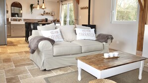 Una sala de estar acogedora, con un sofá color beige, una mesa de centro de madera y una cocina al fondo.