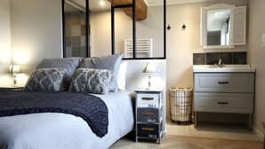 Un dormitorio moderno con una cama grande, lámparas de noche, un aparador con cajones y un espejo sobre el lavabo.