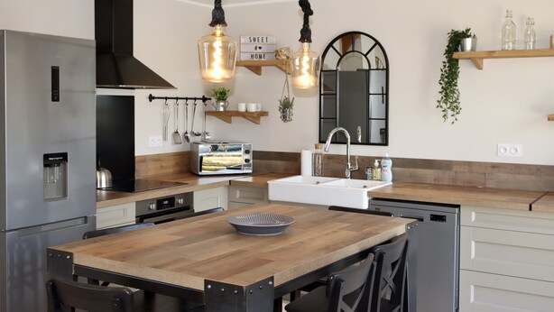Una cocina moderna con una mesa de madera, electrodomésticos de acero inoxidable y lámparas colgantes.