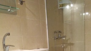 Un baño con lavamanos blanco, inodoro y cabina de ducha con mampara de vidrio.