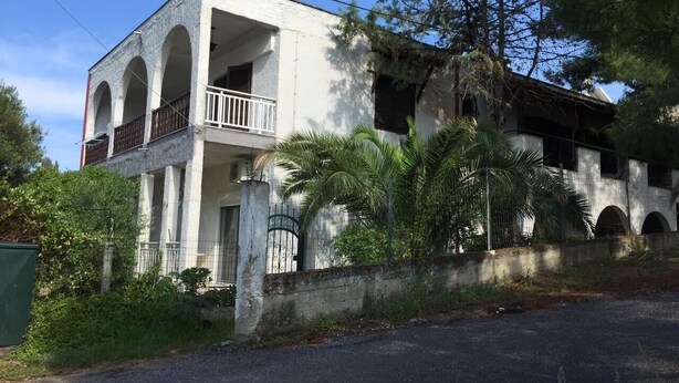 Un edificio de dos pisos con balcón, ventanas arqueadas y entrada protegida por una reja.