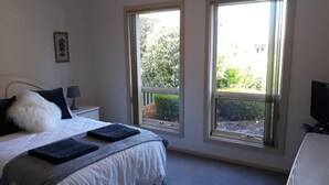 Quarto com cama, duas janelas, mesa de cabeceira, luminária e televisão.