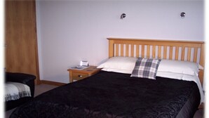A bedroom with a wooden bed, a nightstand, and a chair. - Skara B&B (Thurso)