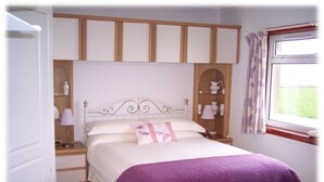 A bedroom with a bed, nightstands, a window with curtains, and a wardrobe. - Skara B&B (Thurso)