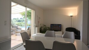 A modern living room with a glass door leading to an outdoor area, a flat-screen TV, and a dining table with chairs. - Air-conditioned Provençal villa in a quiet location with magnificent views. (EGUILLES)