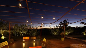 An outdoor dining area with a round table and chairs, surrounded by a wooden deck and potted plants. - Air-conditioned Provençal villa in a quiet location with magnificent views. (EGUILLES)