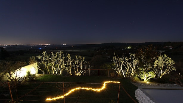 A nighttime view of a landscaped garden with a wooden deck, potted plants, and a light trail. - Air-conditioned Provençal villa in a quiet location with magnificent views. (EGUILLES)