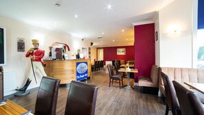 A restaurant with wooden flooring, leather seating, a reception desk, and a statue of a man in a red jacket. - The Douglas Hotel (Kilmarnock)