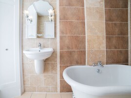 Un baño con bañera independiente, lavamanos sobre pedestal y espejo instalado en la pared con apliques.