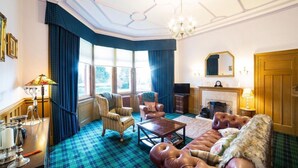 A traditional living room with a checkered floor, leather sofa, armchairs, a fireplace, and a large window with curtains. - The Douglas Hotel (Kilmarnock)