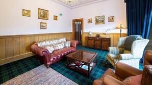 A room with a red leather sofa, a wooden coffee table, a plaid carpet, and a blue curtain. - The Douglas Hotel (Kilmarnock)