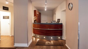 Een receptiebalie met houten afwerking, een klok aan de muur en een bord met de richting naar het toilet.