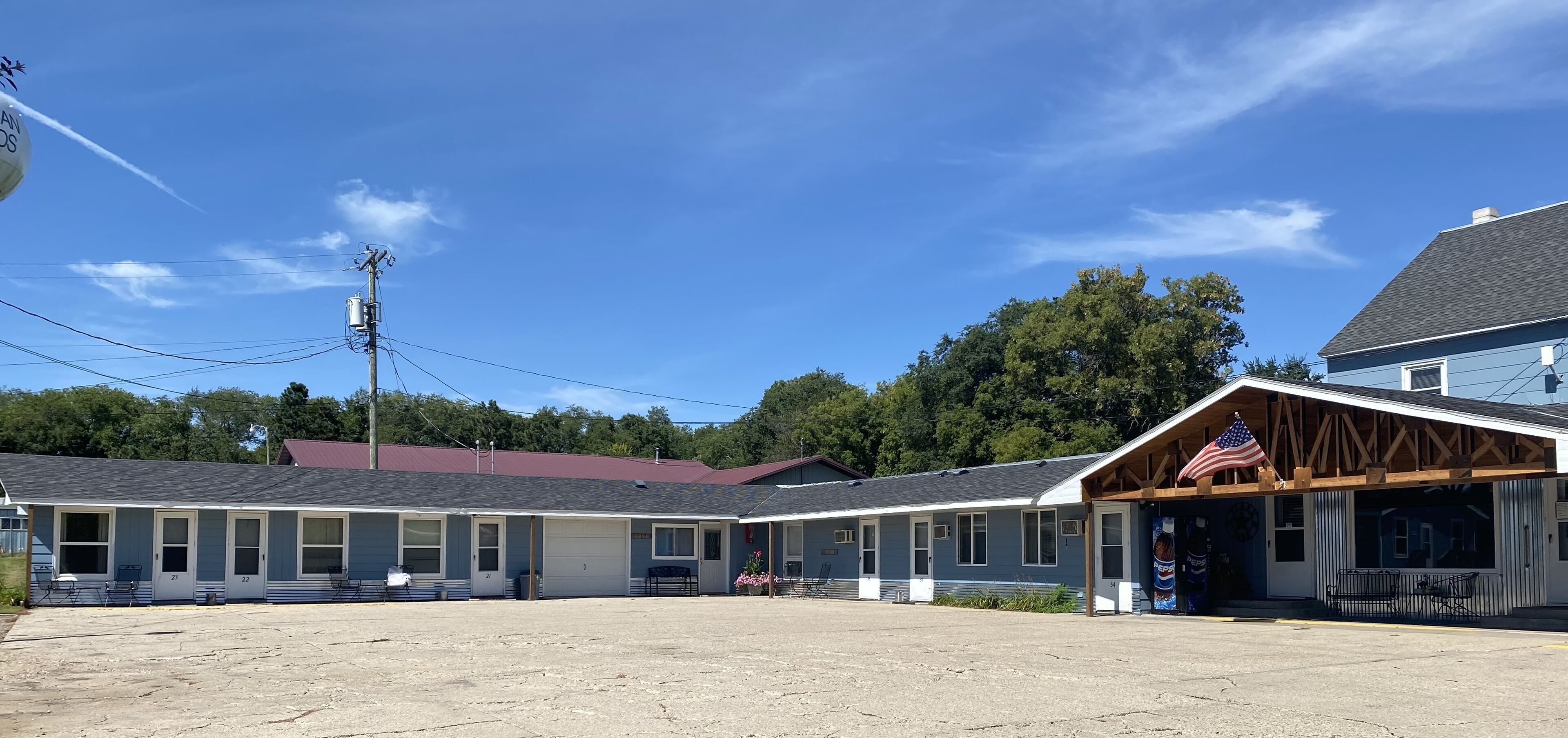 Un motel con habitaciones numeradas, un porche cubierto y una bandera estadounidense.