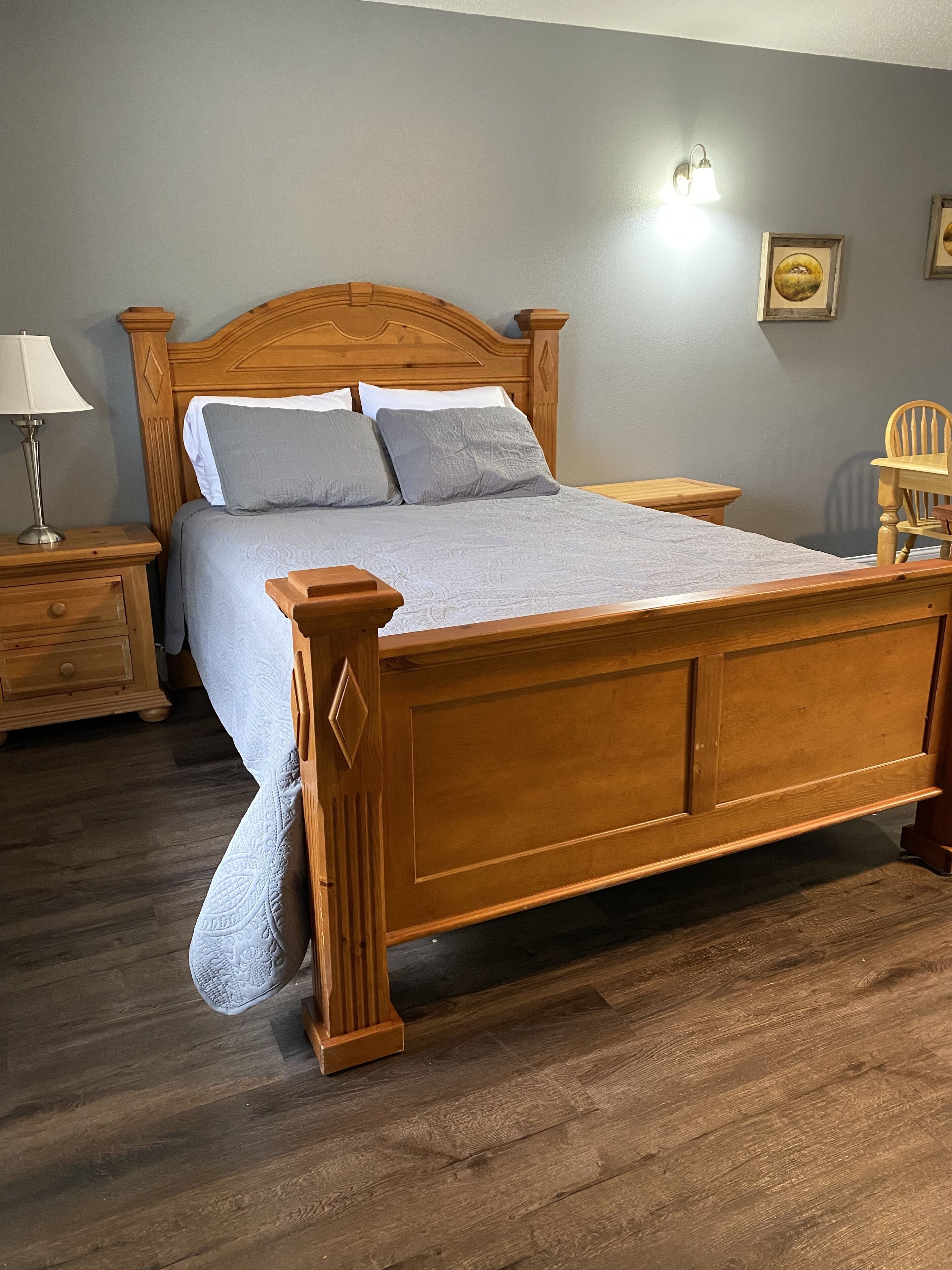 Un lit en bois avec une tête de lit, une table de chevet, une lampe et une chaise.