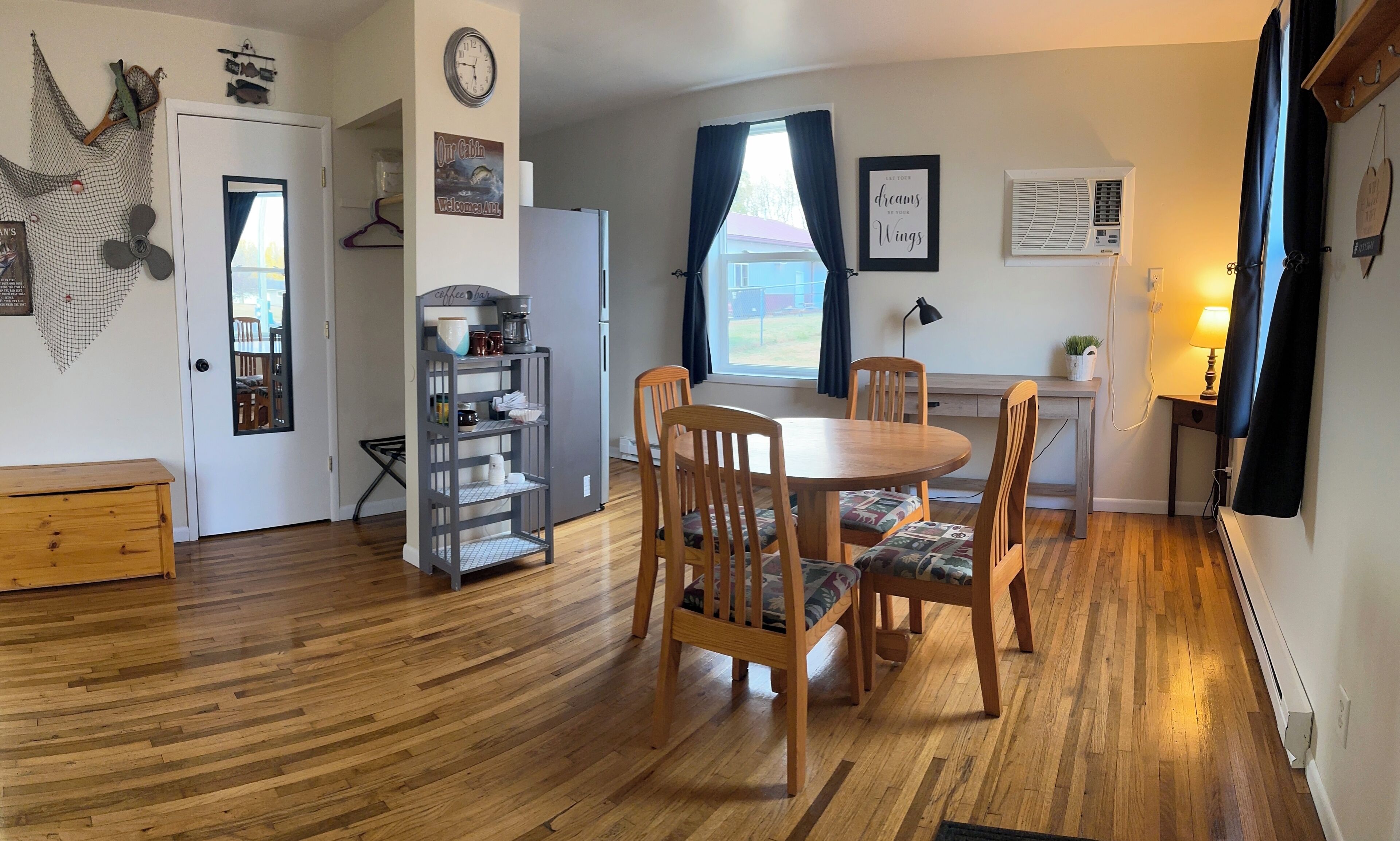 A cozy cabin-style room with a wooden dining table, two chairs, a coffee bar, and a refrigerator.
