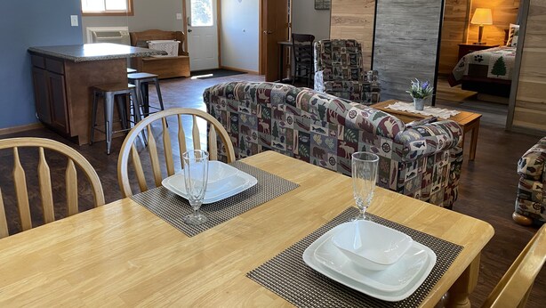 A cozy living room with a sofa, a dining table set with plates and a glass, and a kitchen area with a counter and stools. - Pelican Motel (Pelican Rapids)