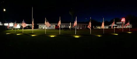 A motel with multiple American flags in front, a neon sign, and a building with a flat roof.