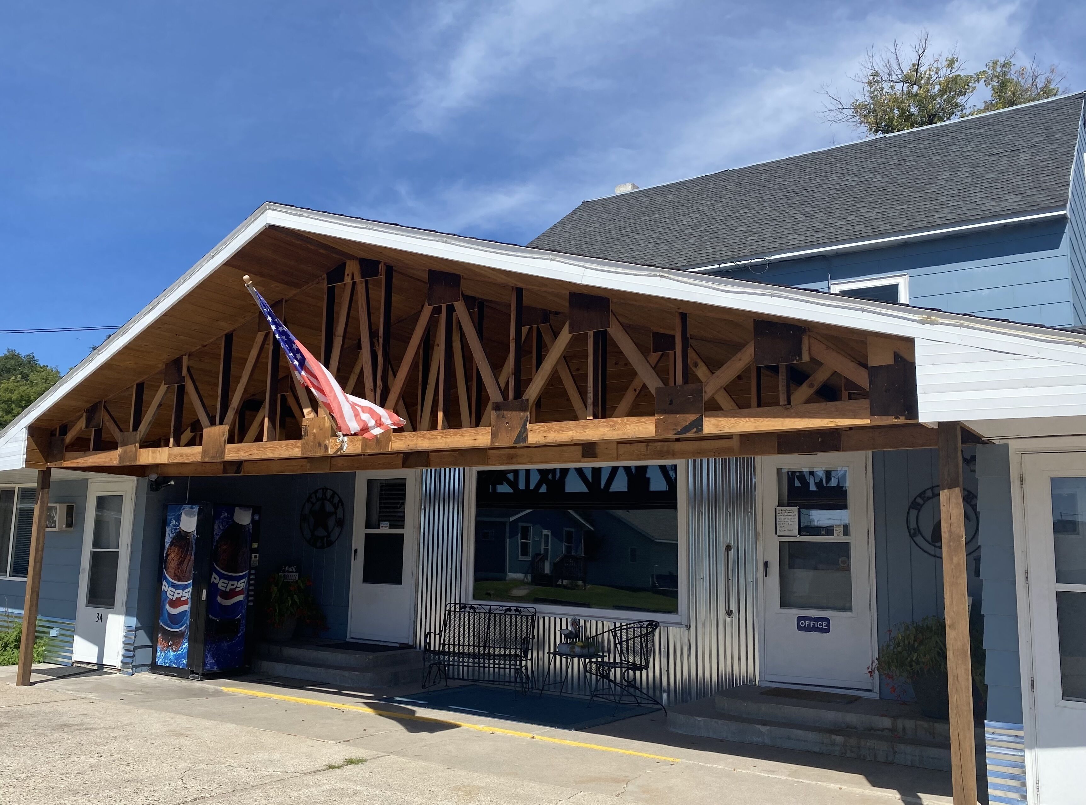 A building with a wooden truss roof, a Pepsi vending machine, and a bench outside.