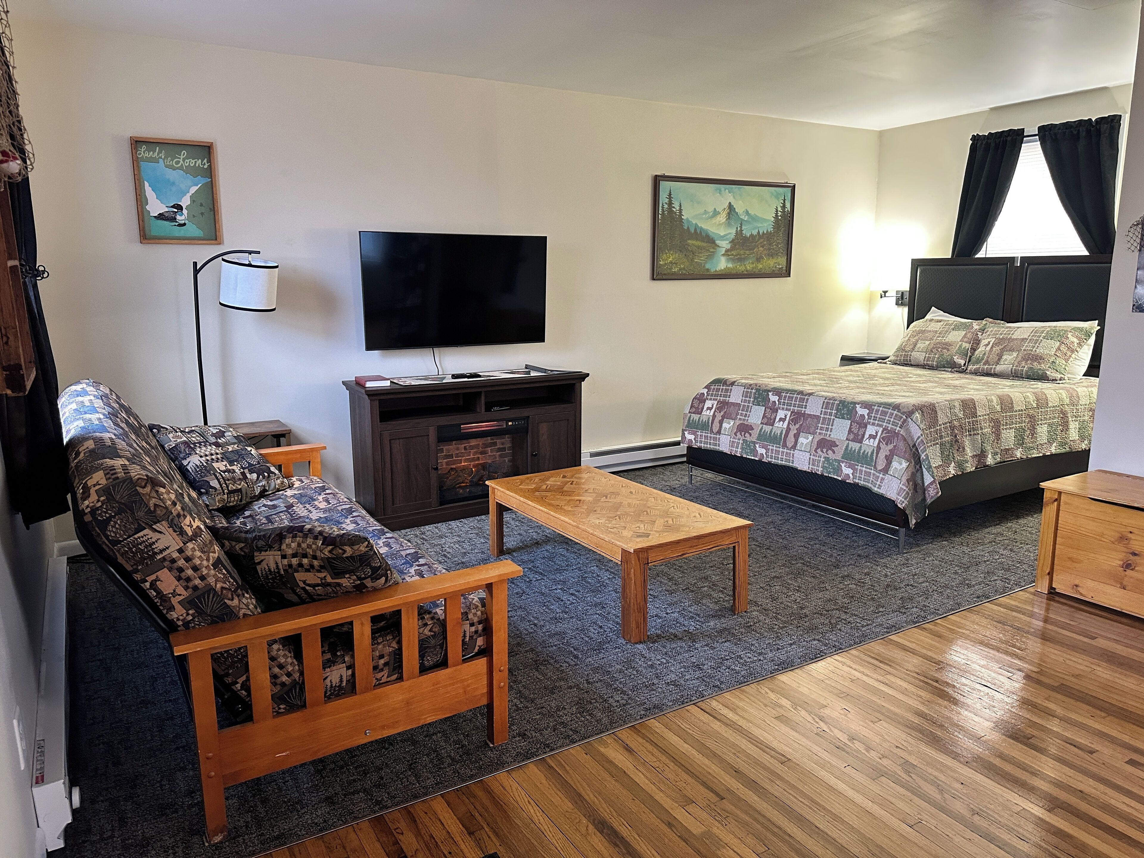Une petite pièce meublée, comprenant un canapé, une table basse en bois, un téléviseur, un lit avec une couvre-lit à motifs et deux tableaux accrochés aux murs.