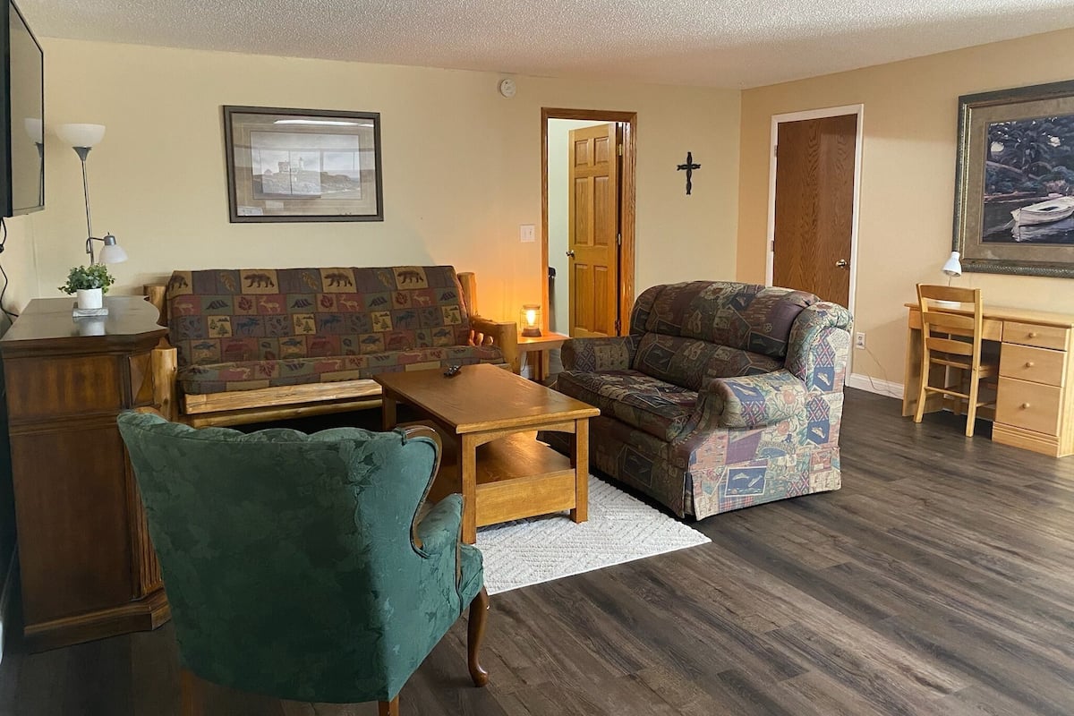 A cozy living room with a sofa, armchair, coffee table, and a desk with a lamp.
