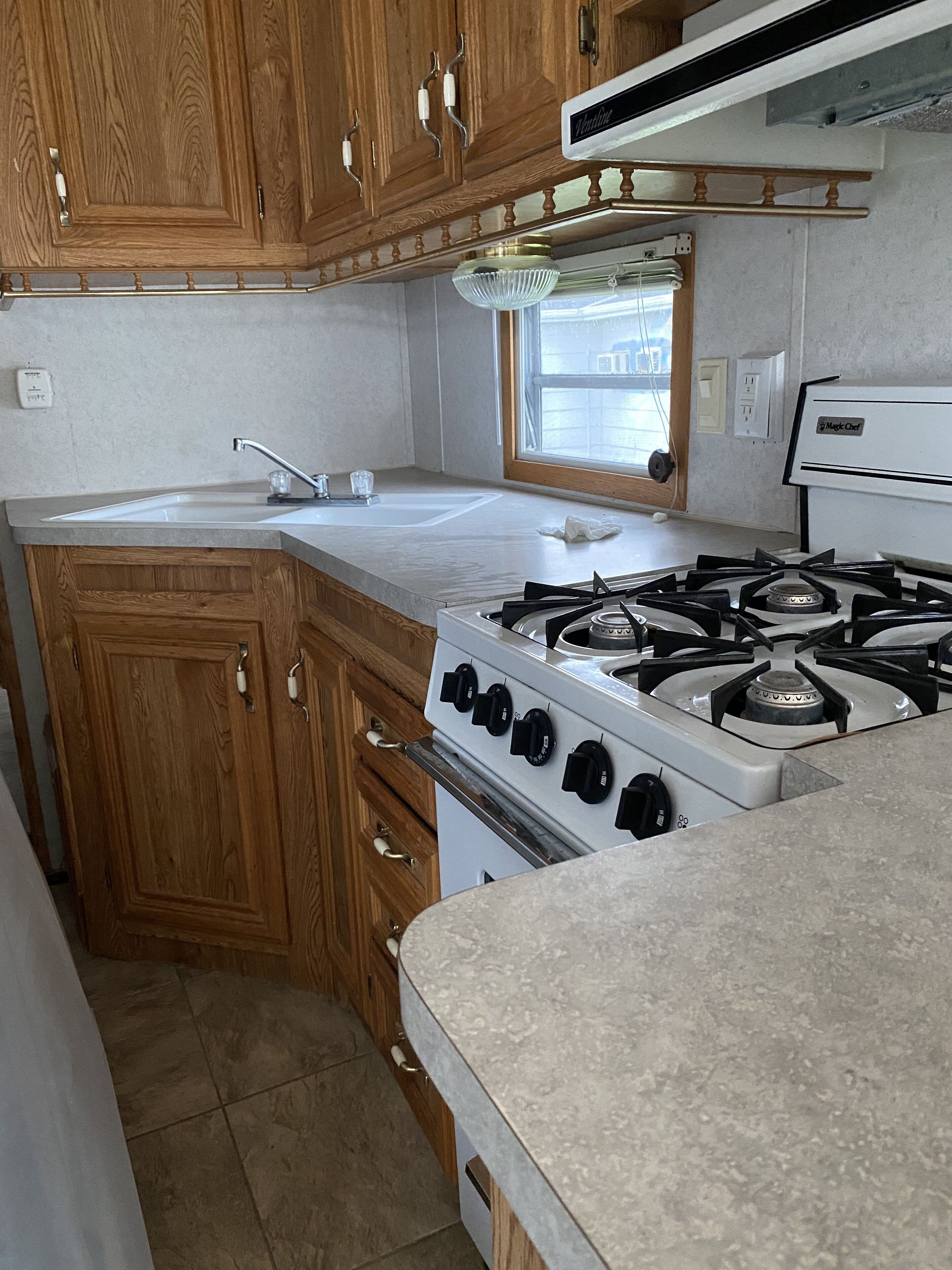 A kitchen with wooden cabinets, a gas stove, a sink, and a window.