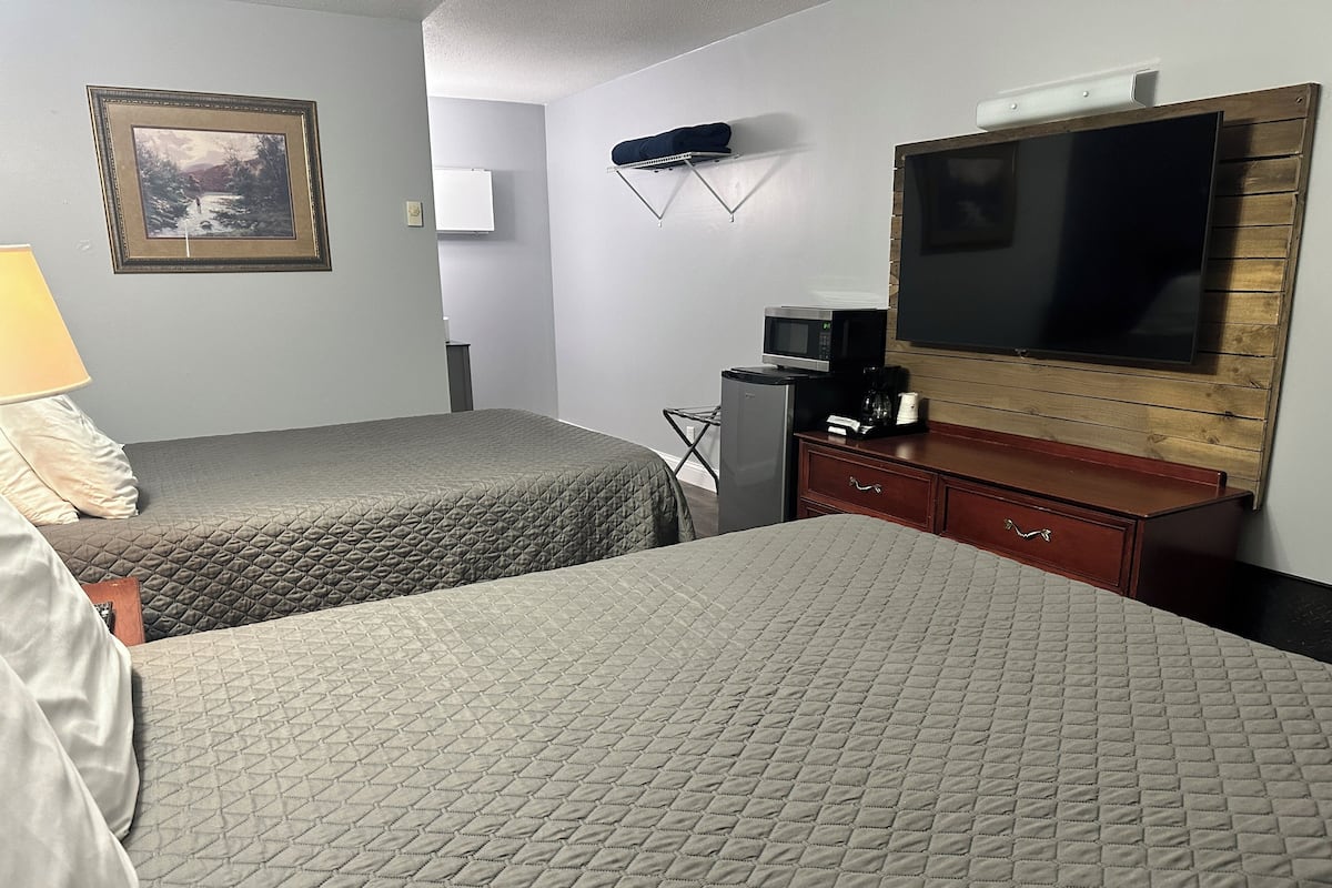 A hotel room with two beds, a TV, a small refrigerator, a microwave, a wooden dresser, and a framed picture on the wall.