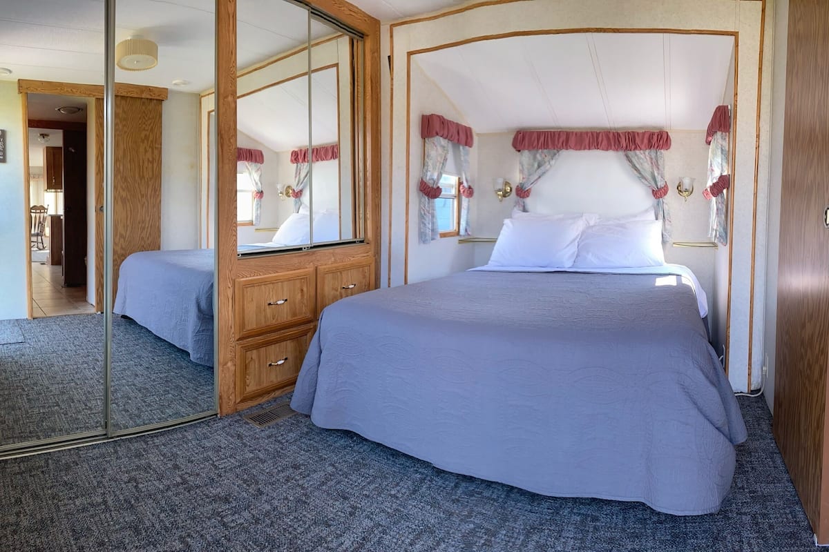 A bedroom with a large bed, a wooden dresser, a mirror, and a wardrobe.